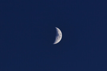 Moon with almost 50% phase on a dark blue sky.