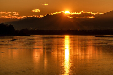 Big sun due sunrise over mountains. Reflcetion on frozen water surface on lake
