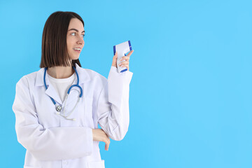 Female trainee doctor with thermometer gun on blue background