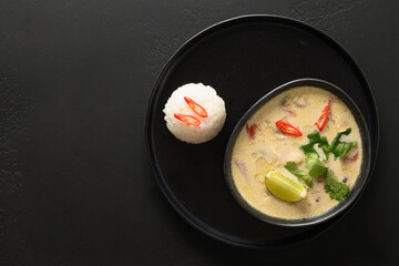 Asian Tom Kha Gai soup with chicken, cherry tomato, coconut milk, kaffir, galangal, lemongrass, mushrooms isolated on black background. Thai food. Coconut Chicken Soup. View from above. Copy space.