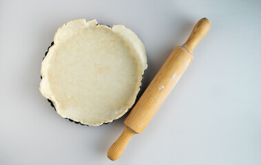 Bakery mold with dough base and wooden rolling pin on white background.