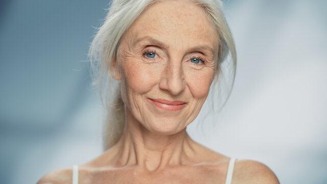 Close-up Portrait Of Beautiful Senior Woman Looking At Camera And Smiling Wonderfully. Gorgeous Elderly Lady With Natural Lush Grey Hair, Blue Eyes. Beauty And Dignity Of Old Age