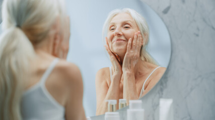 Portrait of Beautiful Senior Woman Morning Routine, Looking into Mirror Gently Applying Face Cream....