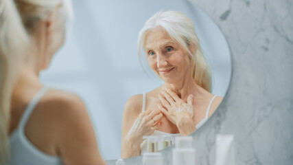 Beautiful Senior Woman Morning Bathroom Routine, Looks into Mirror Touches Her Neck with Sensual Movement of Hands. Elderly Female Natural Beauty. Dignity and Grace in Old Age. Concept for Skin care