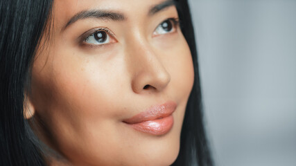 Obraz premium Close-up Portrait Shot of a Beautiful Asian Woman Looking Up. Young Adult Female with Lush Black Hair With Clean Soft Skin. Close-up Portrait