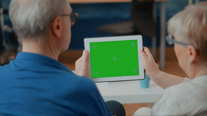 Old couple looking at green screen template on digital device, analyzing blank copy space and...