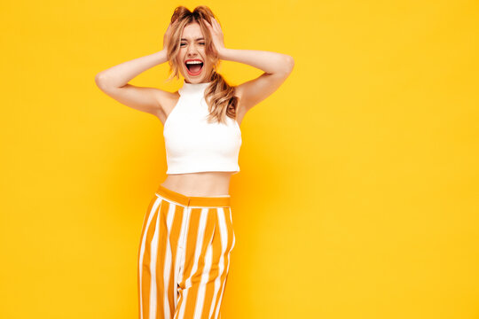 Portrait of young beautiful smiling blond female in trendy summer clothes. carefree woman posing near yellow wall in studio. Positive model having fun indoors. Cheerful and happy.Screams and shouts