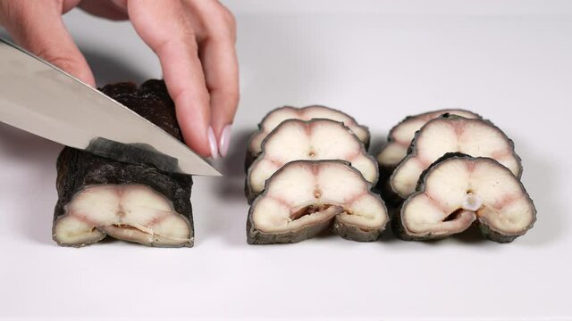 Closeup view 4k stock video footage of tasty cooked smoked eel fish isolated. Woman cuts fish on white plastic chopping board background using knife