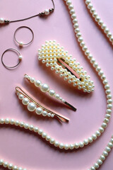 Various pearl jewelry and hair accessories on pink background. Flat lay.