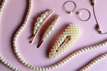 Various pearl jewelry and hair accessories on pink background. Flat lay.