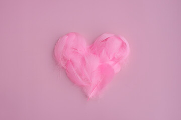 Heart shape made of bright pink feathers and fluff on pink background. Valentines day, romantic love