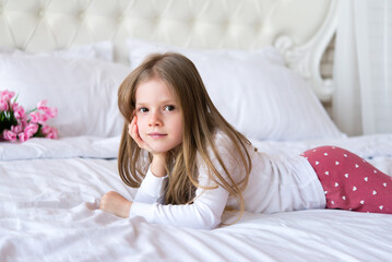 girl in pajamas lies on a bed with white linens. Floral decor.