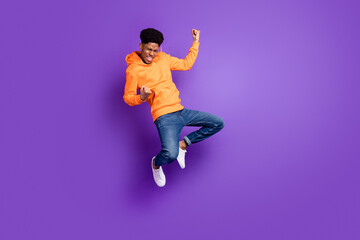 Fototapeta na wymiar Full length photo of young crazy dark skin man jump up air fists winner celebrate isolated on violet color background