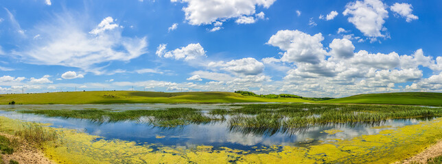 Obraz na płótnie Canvas Lake and green fields panorama, blue sky and fluffy clouds - wallpaper