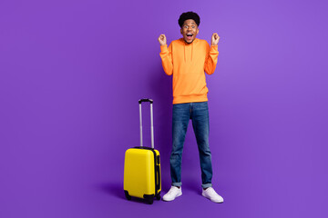 Full body photo of cheerful young happy afro american man winner luggage wear jeans hoodie isolated on purple color background