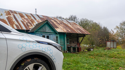 Part of a modern electric car on the background of an old village house. The concept of old and new.