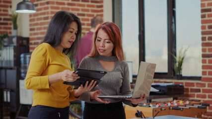 Business people doing teamwork in startup office. Asian women using laptop and digital tablet to create marketing presentation for company growth. Partnership and productivity.