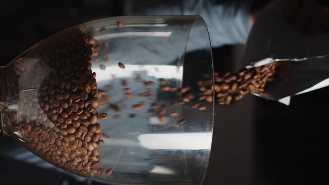 Close up of barista pours coffee beans into a coffee grinder from package in slow motion. Vertical video template for smartphone web promo.