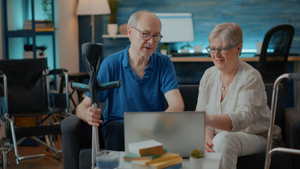 Obraz premium Senior people giving high five and celebrating successful teamwork on laptop at home. Retired man and woman with disability feeling positive about success on computer. Walking support