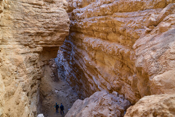 View inside a deep dry canyon in a remote desert region. High walls of a narrow canyon of wadi Hava in the Negev Desert. Hikers on hiking trail in a heart of the desert. 