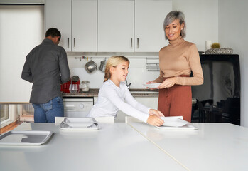 Obraz premium Family consisting of father, mother and daughter setting the table to eat in the kitchen.