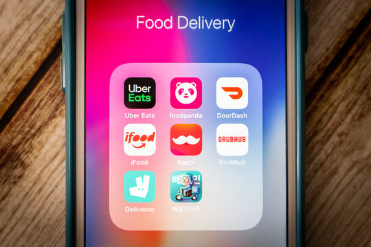 Kumamoto, JAPAN - Jun 8 2021 : Online food delivery and ordering platform icons (Uber Eats, Foodpanda, DoorDash, iFood, Rappi, Grubhub, Deliveroo and Baedal Minjok) on iPhone on chic shabby table