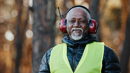 Elderly man professional forestry engineer in protective soundproof headphones standing in forest looking at camera mature african american foreman sawmill worker in uniform smiling posing outdoors