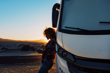 People on travel with modern camper. Woman using mobile phone roaming against big motorhome....