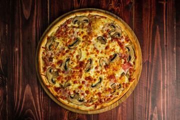 An overhead view of mushroom and ham pizza with cheese and tomato sauce on a wooden tray and table. - Powered by Adobe