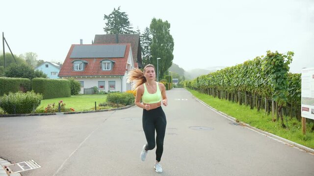 Caucasian cheerful young beautiful fit woman running on street outdoors. Pretty happy sportswoman jogging outside, cardio workout. Sporty healthy lifestyle, athletic concept