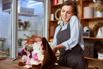 Busy florist wrapping fresh bouquet and answering phone