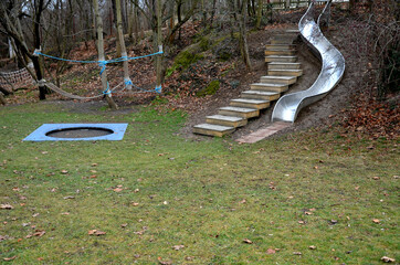 stainless steel slide on the playground with concrete hills and rocks and wooden staircase. Large...