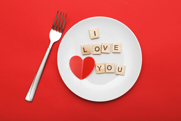 inscription i love you with a heart on a white plate with fork on red background