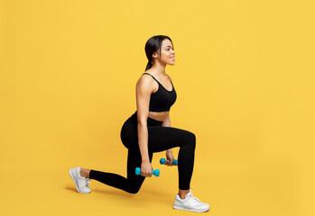 Fototapeta na wymiar Strength training concept. Athletic black lady doing lunges exercise with dumbbells on yellow background