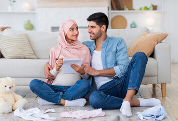 Young pregnant islamic couple getting ready for childbirth, making checklist of necessities while sitting on floor