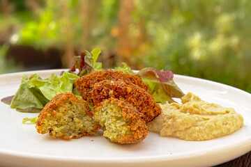Three falafel balls, one cut, humus and salad on a plate, selective focus