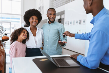 Salesman giving new car key to young Afro family at auto dealership. Vehicle local distribution concept