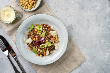 grey porcelain scandi soup bowl with traditional east european dish buckwheat salad with butter and chickpeas on concrete surface and kitchen towel, top view, copy space