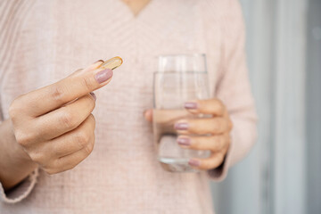 woman hand taking fish oil with a glass of water closeup