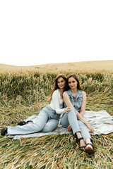 Naklejka na ściany i meble two sisters are sitting on a blanket at sunset in a field. girlfriends have fun together, happy girls. sisters hug.