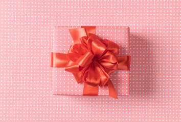 Pink gift box with a bow on a red background. Close-up. Top view