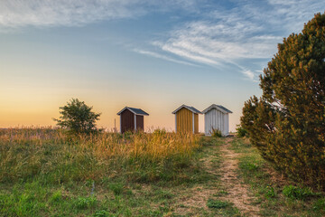 Three small rustic summerhouses at sunset on a strand show nordic summer vacation or Scandinavian...