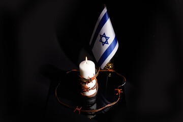 Barbed wire on burning candle and Israel flag on black background with space for text. Holocaust...