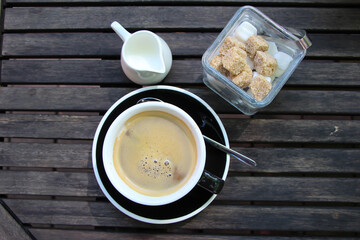 front top photo cup of freshly brewed coffee on a brown wooden table with a milk pot and sugar bowl 
