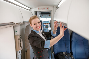 Cheerful flight attendant checking overhead shelf in airplane