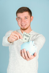 Fototapeta na wymiar A red-haired, bearded man puts a hundred-dollar bill in a blue piggy bank, selective focus