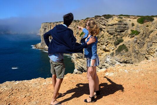 Young couple enjoying beauty of Atlantic Ocean shore, monumental cliffs near Cape St. Vincent, Vicentine Coast, Sagres, Vila do Bispo, Faro district, Algarve, Portugal, Europe