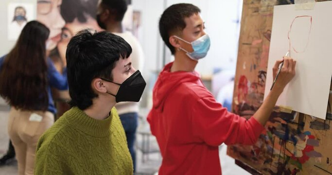 Multiracial students painting inside art room class wearing safety masks - School and healthcare concept