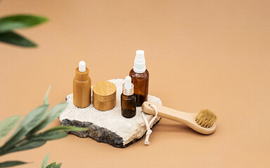 Blank amber glass and bamboo essential oil bottles with pipette, glass spray bottle and bamboo jar on natural stone podium. Organic spa cosmetic beauty product mock up.