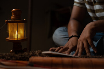 unrecognizable Young student busy reading during night under oil lamp or lantern due to power loss and Poverty - concpet of power cut, blackout, electricity failure during examination. - obrazy, fototapety, plakaty